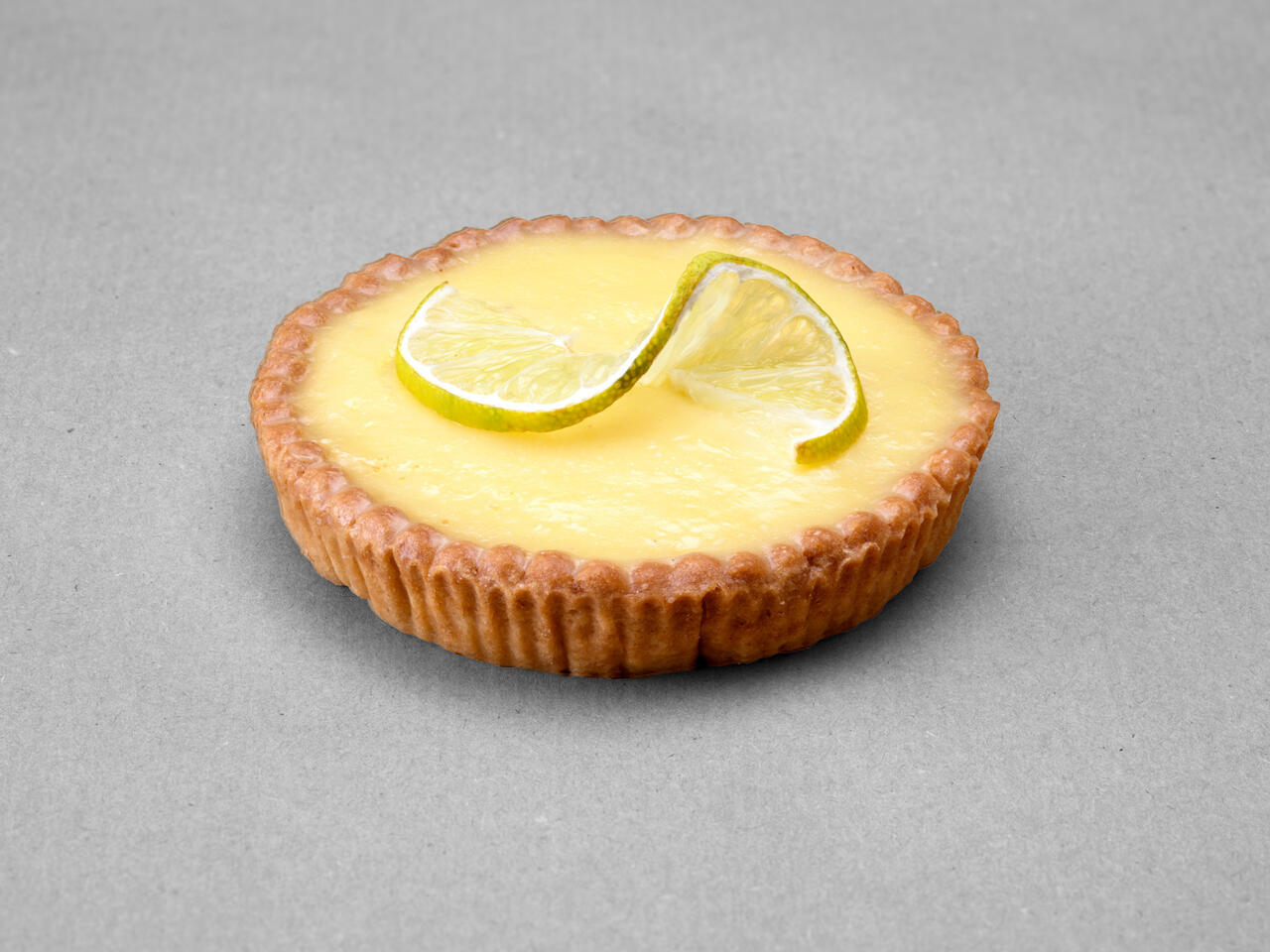 Tartelette citron posée sur fond gris avec comme décor une tranche de citron coupée