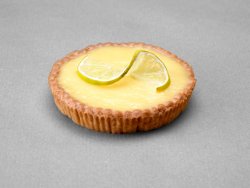 Tartelette citron posée sur fond gris avec comme décor une tranche de citron coupée