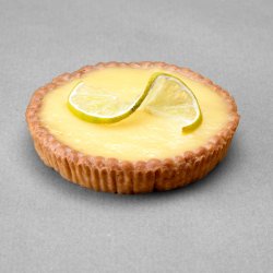 Tartelette citron posée sur fond gris avec comme décor une tranche de citron coupée